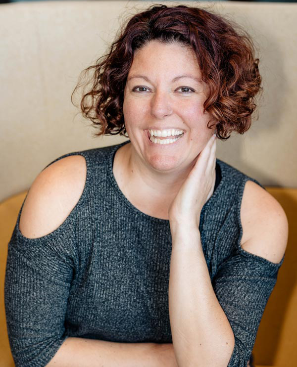 Smiling woman in gray top, curly hair.